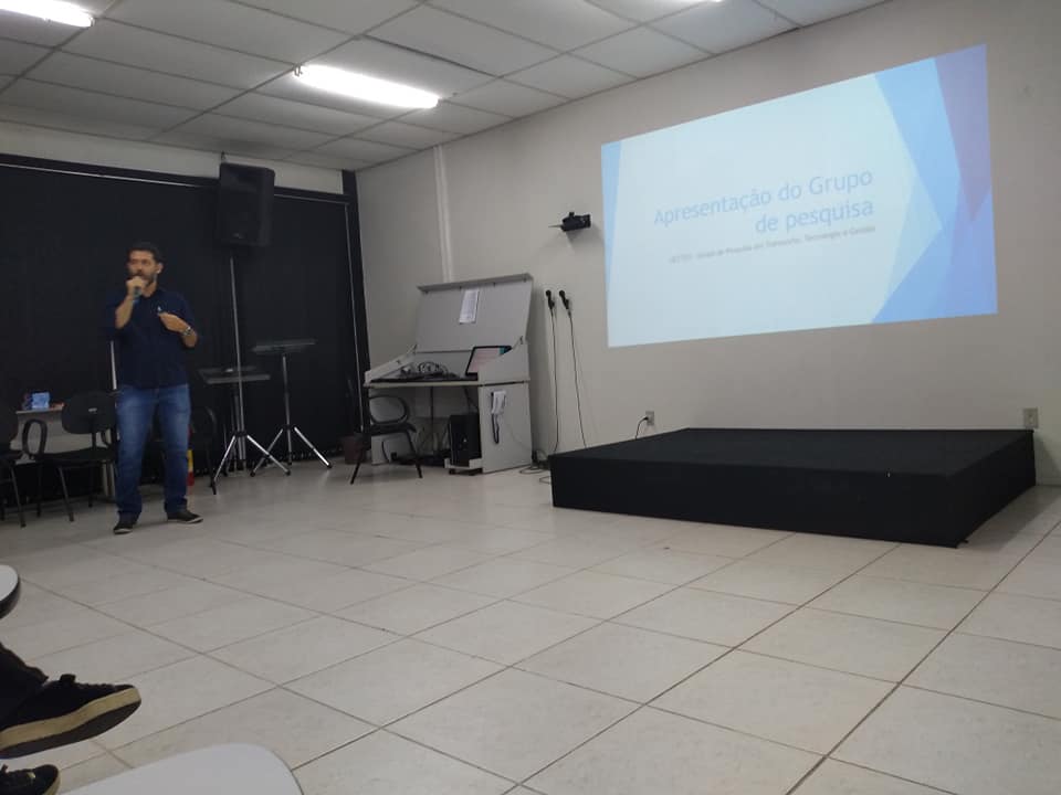 #pratodosverem Foto de um homem de camisa azul em pé com um microfone na mão. Ao fundo as bandeiras de Volta Redonda, Brasil e Estado do Rio de Janeiro